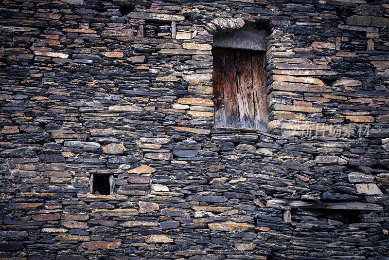 Side Of A Stone House With A Wooden Door and SmClose photo Of A old Stone building的一面。